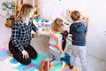 Little kids and educator studying numbers and alphabet on magnetic board sitting on floor in playroom backview