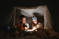 Little kids involving in reading amazing book. They lying in nice toy tent in playroom. Boy holding flashlight in hand.