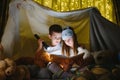 Little kids involving in reading amazing book. They lying in nice toy tent in playroom. Boy holding flashlight in hand.