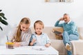 little kids painting at table while their grandfather reading book behind on sofa Royalty Free Stock Photo