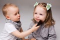 Little kids sitting, playing at studio with cosmetics, boy making makeup for pretty blonde girl with two tails. Children Royalty Free Stock Photo