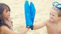 Little kids with snorkeling equipment sitting on sand on tropical beach and playing with flippers on hands. Royalty Free Stock Photo