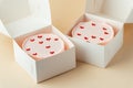 Little Korean style pink bento cake with hearts in a white box on the beige background. Pastry as a gift for a birthday of