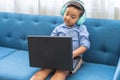 Little latin boy with headphones using a laptop sitting on a blue sofa Royalty Free Stock Photo