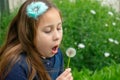 Little latina girl in garden blowing on dandelion