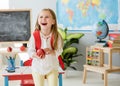 Little laughing blond girl holding an apple in the school classroom