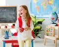 Little laughing blond girl holding an apple in the school classroom