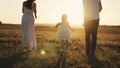 a little laughing girl runs with her parents at sunset, a happy family, a childhood dream, kid running in sunshine with Royalty Free Stock Photo