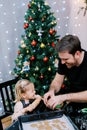 Little laughing girl sits near her dad cutting out cookies with dough cutters on the table Royalty Free Stock Photo