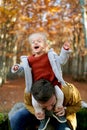 Little laughing girl sits waving her hands on the shoulders of her dad, who leaned forward