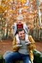 Little laughing girl sits waving her hands on the shoulders of her laughing dad in the park