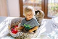 Little laughing girl sitting in a cat bed next to a sitting cat on the bed Royalty Free Stock Photo