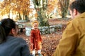 Little laughing girl under falling leaves stands in front of mom and dad in the autumn park. Back view Royalty Free Stock Photo