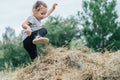 Little laughing girl 3-4 years old jumps and plays in hay stack, on background of trees Royalty Free Stock Photo