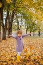 Little laughing pretty girl with blond hair in red purple dress throws yellow leaves in autumn park Royalty Free Stock Photo