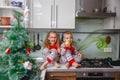 Little laughing twins sit on the table in pajamas in the Christmas decorated kitchen with an Apple. Girl with glasses Royalty Free Stock Photo