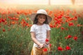 Little longhaired girl in hat posing at field of poppies with  on summer sun Royalty Free Stock Photo