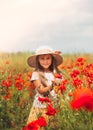 Little longhaired girl in hat posing at field of poppies with  on summer sun. Vertical Royalty Free Stock Photo