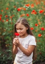 Little longhaired girl posing at field of poppies with on summer sun. Vertical