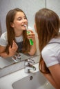 Little lovely girl brushing her teeth with electric toothbrush looking at her reflection in mirror in bathroom Royalty Free Stock Photo