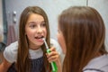 Little lovely girl brushing her teeth with electric toothbrush looking at her reflection in mirror in bathroom Royalty Free Stock Photo