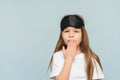Little lovely girl wearing a sleep mask yawns over isolated blue background, studio shot, child getting ready for bed Royalty Free Stock Photo