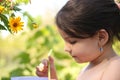 Little lovely smiling girl picks a straw in a glass while sitting at a summer table on a blurred natural background