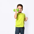 Little male in yellow t-shirt and denim shorts. He smiling, lifting green dumbbell, posing isolated on white studio background Royalty Free Stock Photo