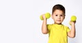 Little male in yellow t-shirt and denim shorts. He smiling, lifting dumbbell, posing isolated on white studio background Royalty Free Stock Photo