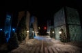 Little miniature city with road and lights. Decorative cute small houses in snow at night in winter. Creative Holiday concept.