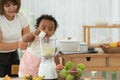 Little mixed race child girl, African and Asian, and her mother making healthy fruits smoothie together in kitchen at home. Cute Royalty Free Stock Photo