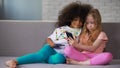 Little multi-ethnic sisters on couch, hugging and taking photos on smartphone