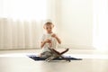 Little Muslim boy with misbaha and Koran praying on rug