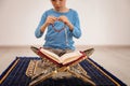 Little Muslim boy with misbaha and Koran praying on rug indoors