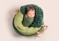 Nwborn swaddled in green coccon lying on basket