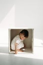 A little one-year-old girl is playing, climbed into a wooden cube - a chair