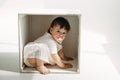 A little one-year-old girl is playing, climbed into a wooden cube - a chair