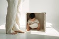 A little one-year-old girl is playing, climbed into a wooden cube - a chair