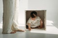 A little one-year-old girl is playing, climbed into a wooden cube - a chair