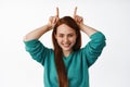 Little party never kill nobody. Funny redhead woman looks happy, shows bull horns devil gesture and playing, smiling