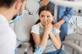 Little patient with toothache and male doctor sitting in dental chair while mother standing near her for support Royalty Free Stock Photo