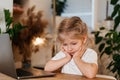 little pensive blonde girl sitting in front of a laptop with a sad face the concept of home schooling and loneliness Royalty Free Stock Photo