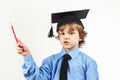 Little pensive boy in academic hat with pencil on white background