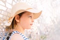 Little pensive girl in a straw hat standing against the background of a bright wall