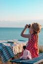 Child girl in a straw hat red polka-dot dress on vintage bench taking a picture of soft pink rabbit toy on sea lanscape Royalty Free Stock Photo