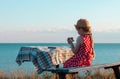 Child girl in a straw hat red polka-dot dress on vintage bench taking a picture of soft pink rabbit toy on sea lanscape Royalty Free Stock Photo