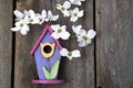 Little pink, purple and yellow birdhouse on rustic fence