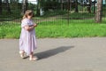 Little plump girl walks along a deserted park path, looking at a smartphone