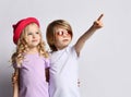 Little positive blond baby girl and boy in stylish clothing standing, hugging each other and pointing at something above Royalty Free Stock Photo