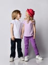 Little positive blond baby girl and boy in stylish casual clothing and accessories standing and looking at each other Royalty Free Stock Photo